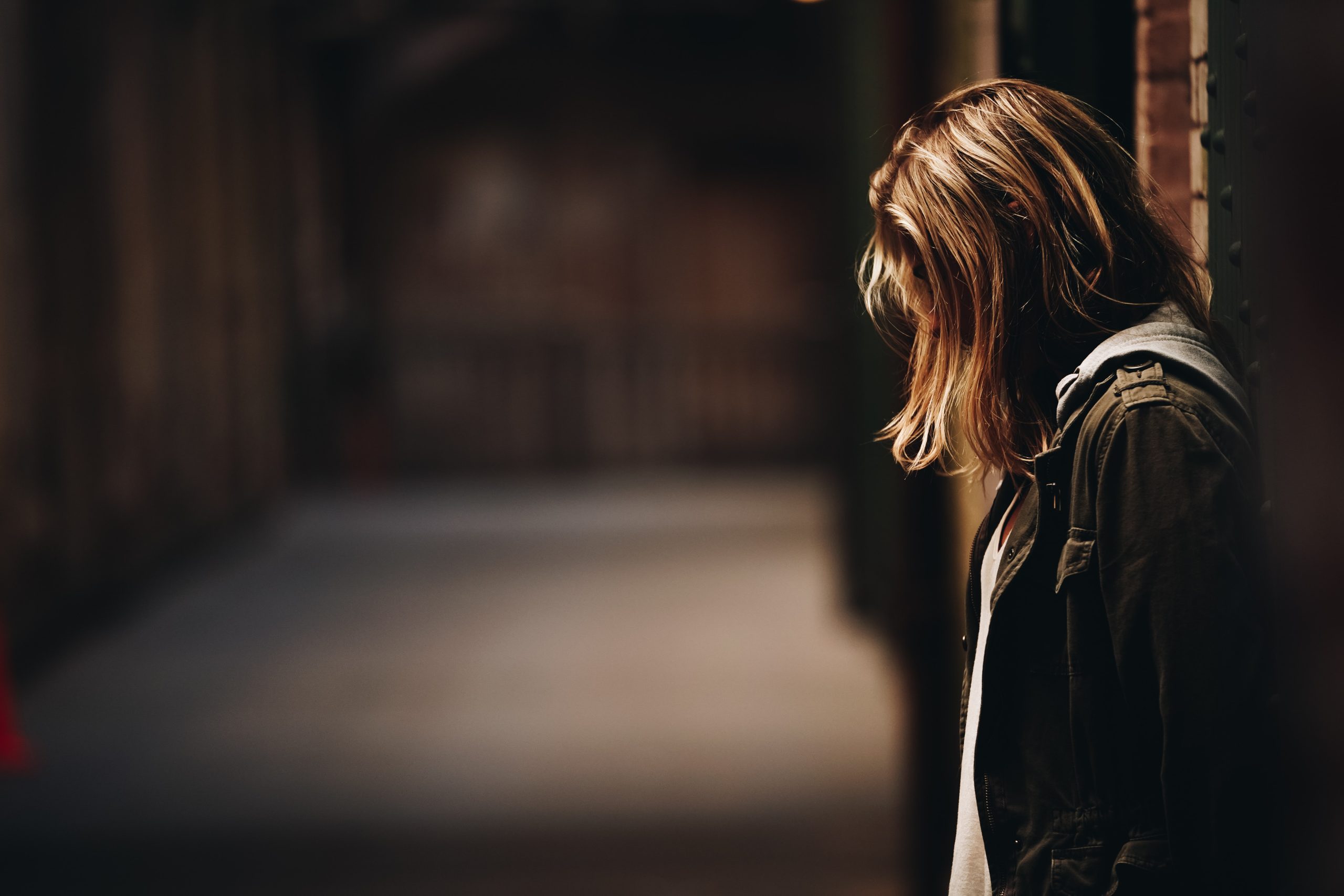 Girl with brown hair, leaning against a wall in dim hallway, head down, face hidden with hair - Personality Disorders