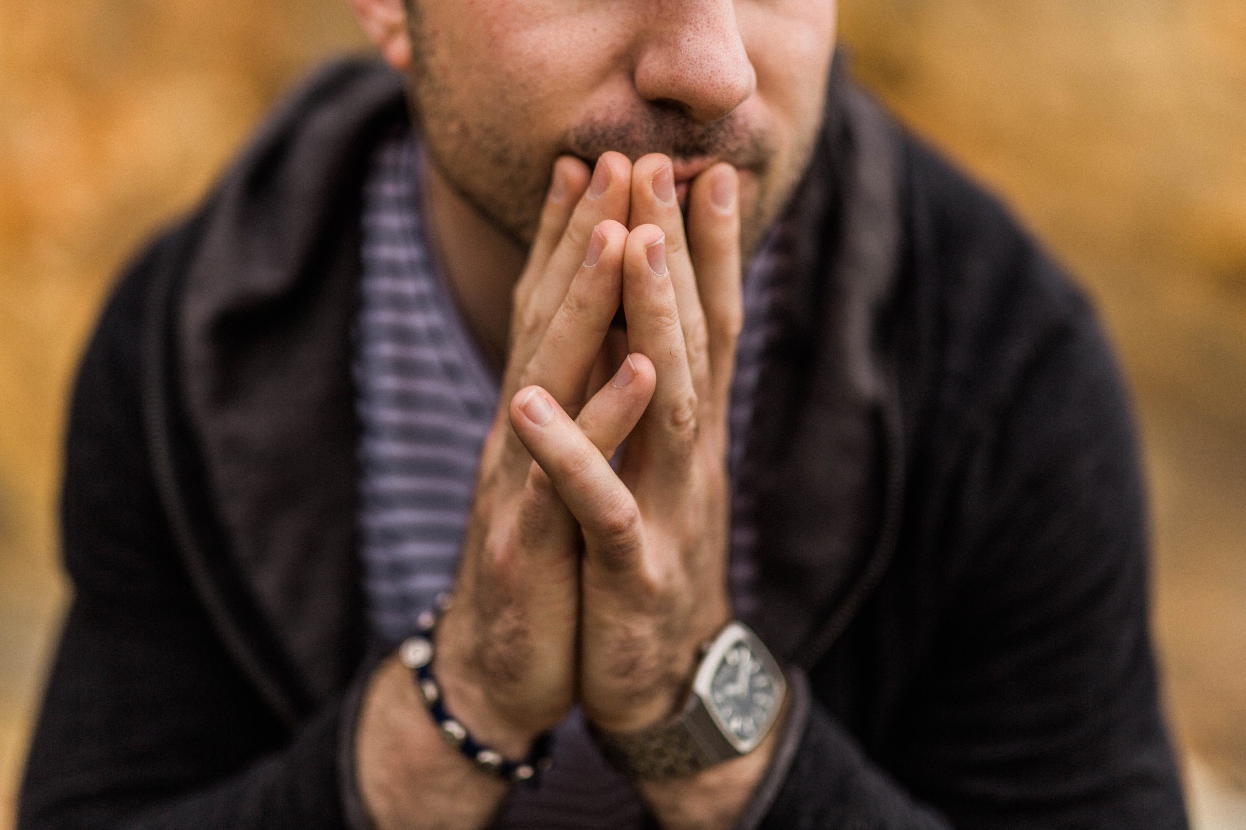 Man touching palms of his hands to each other while some fingers cover his mouth