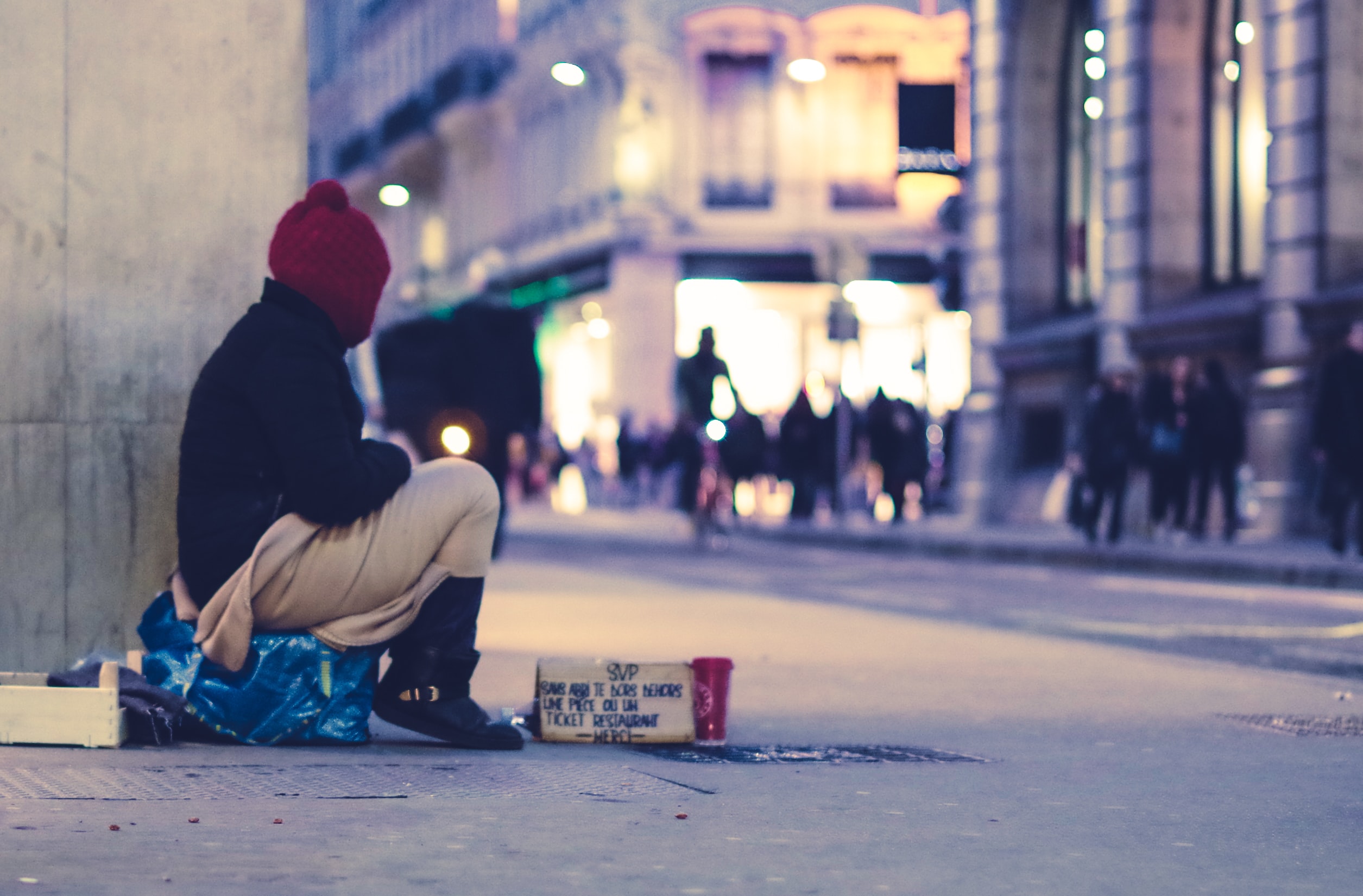 Needy person sitting beside the building, looking across the street 