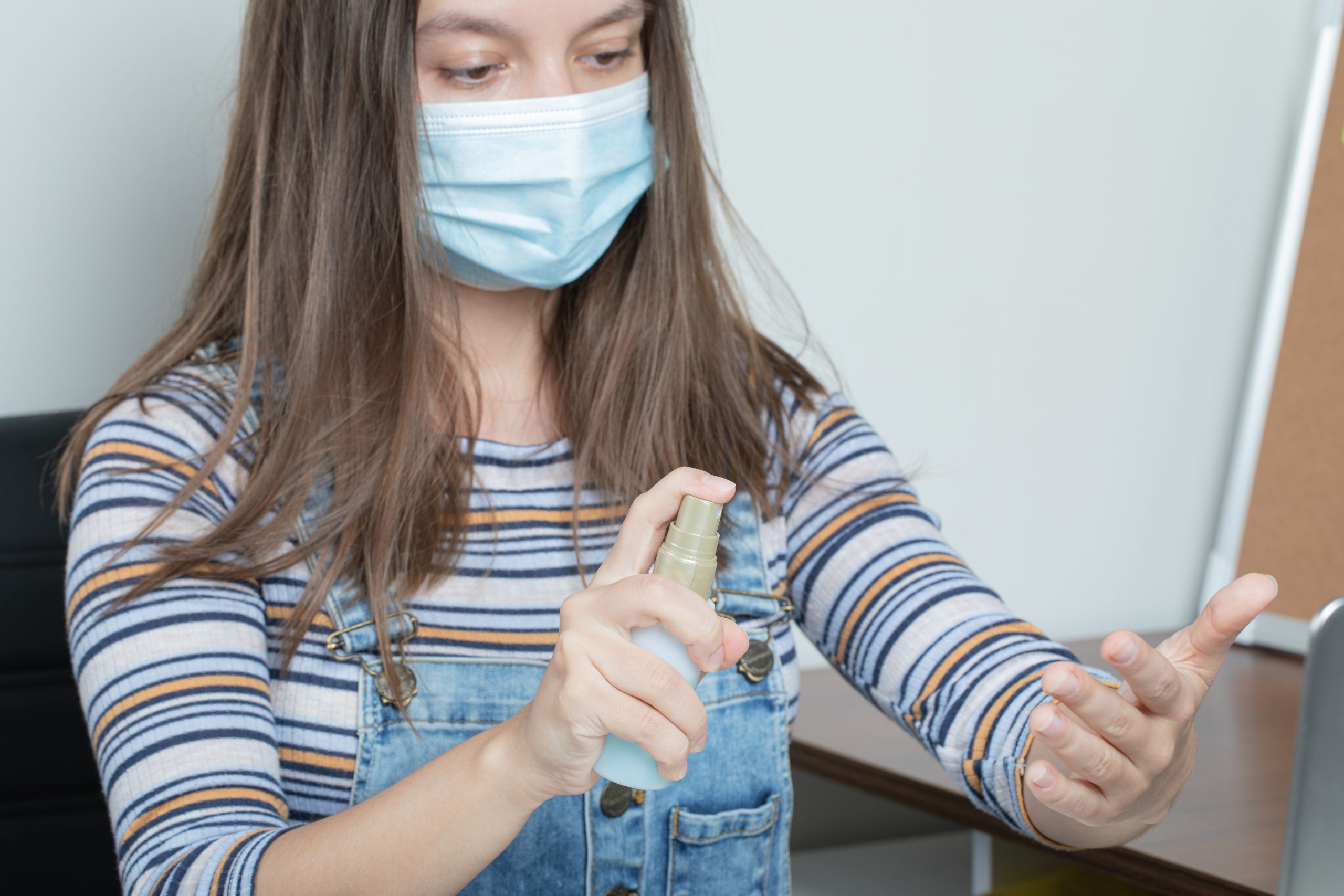 Girl with mask on her face, sanitizing her hand