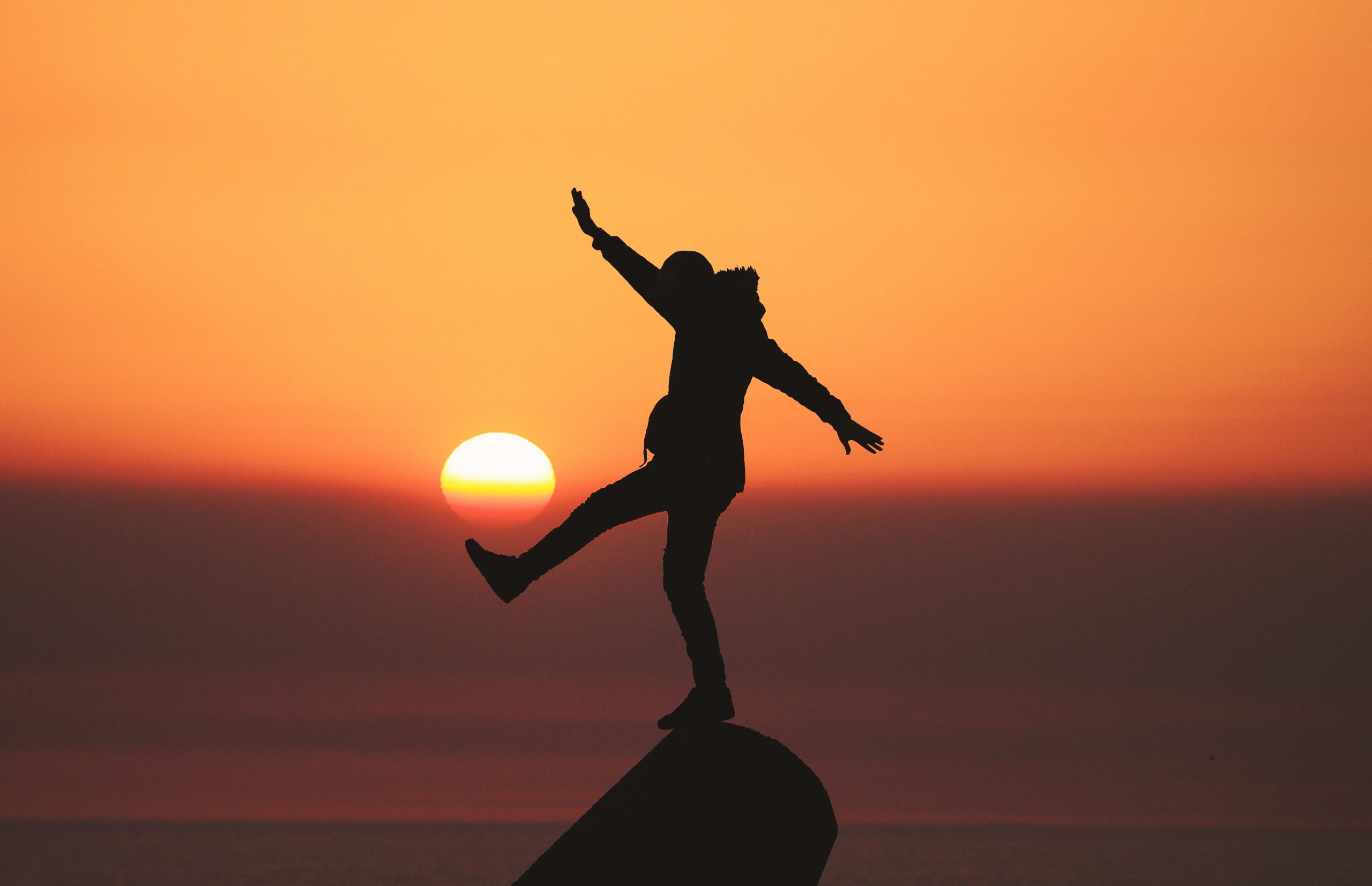 Silhouette of a man balancing himself on one foot on a rock