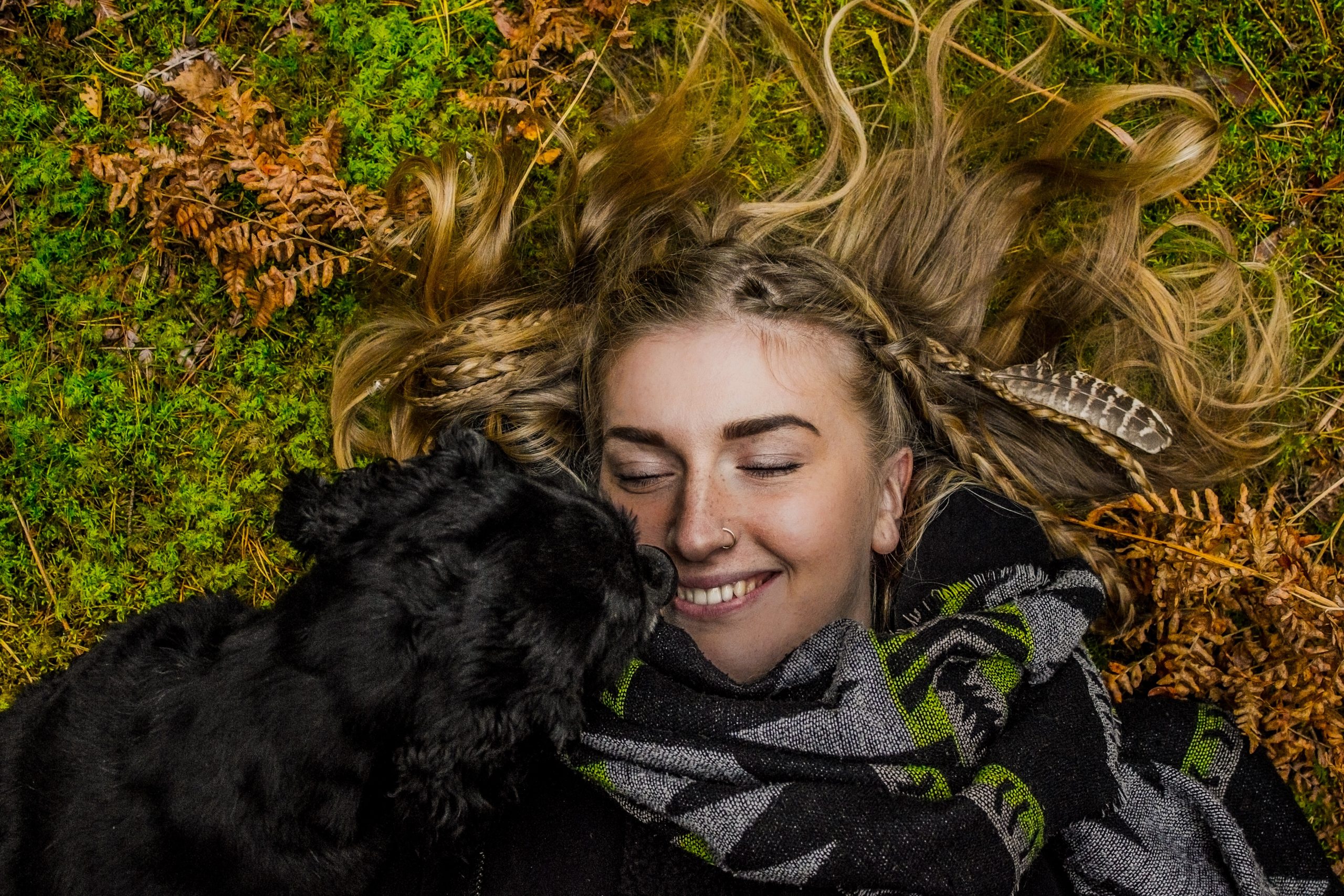 A woman lying on grass, smiling, her eyes closed and a black dog near her. - Self-care tips for mental health