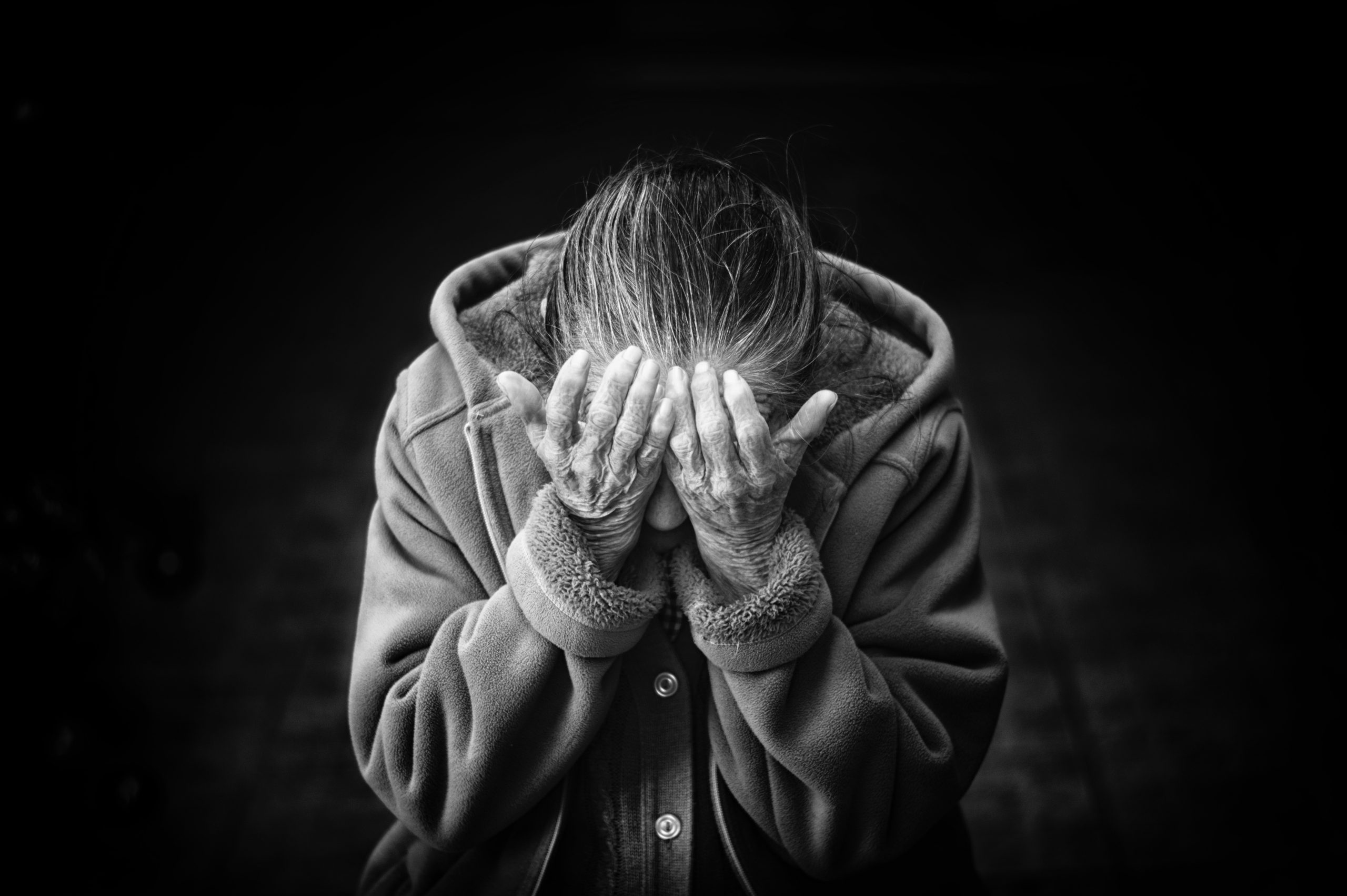 Black and white picture of old woman covering her face with hands