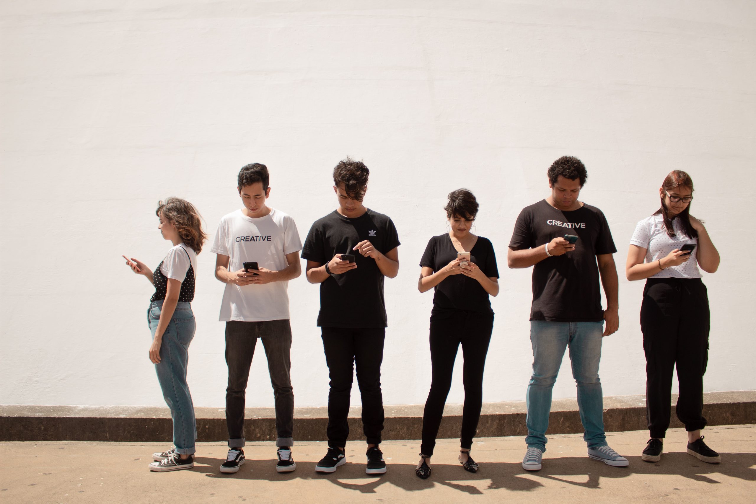 A group of young people, standing together but all looking into their smartphones
