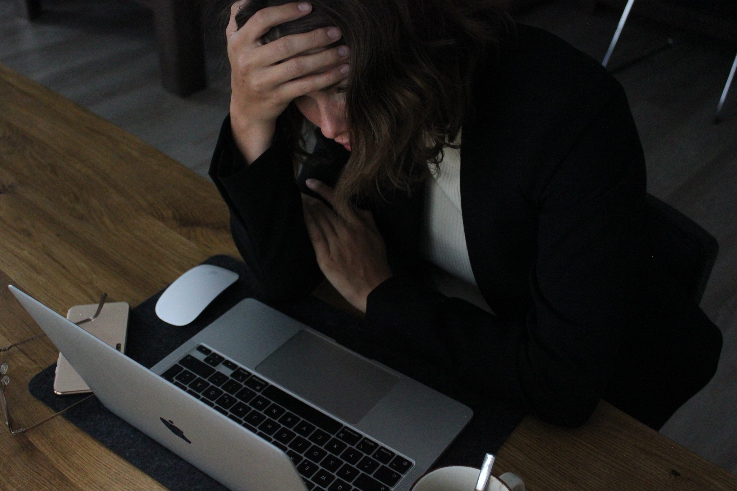 A stressed woman, holding her hand with hand, sitting in front of laptop