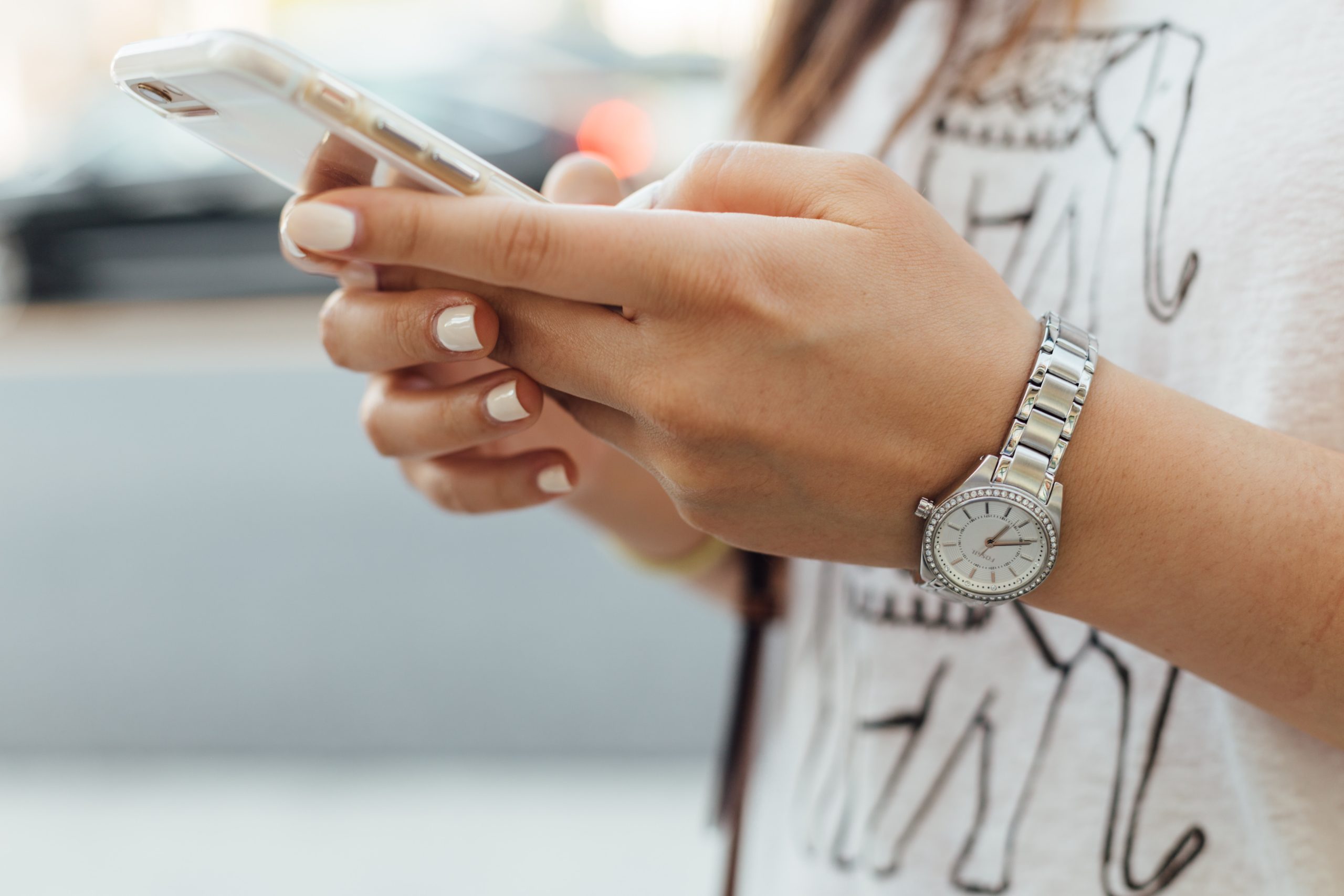 Girl in white shirt, white nailpaint, holding a smartphone in hands.