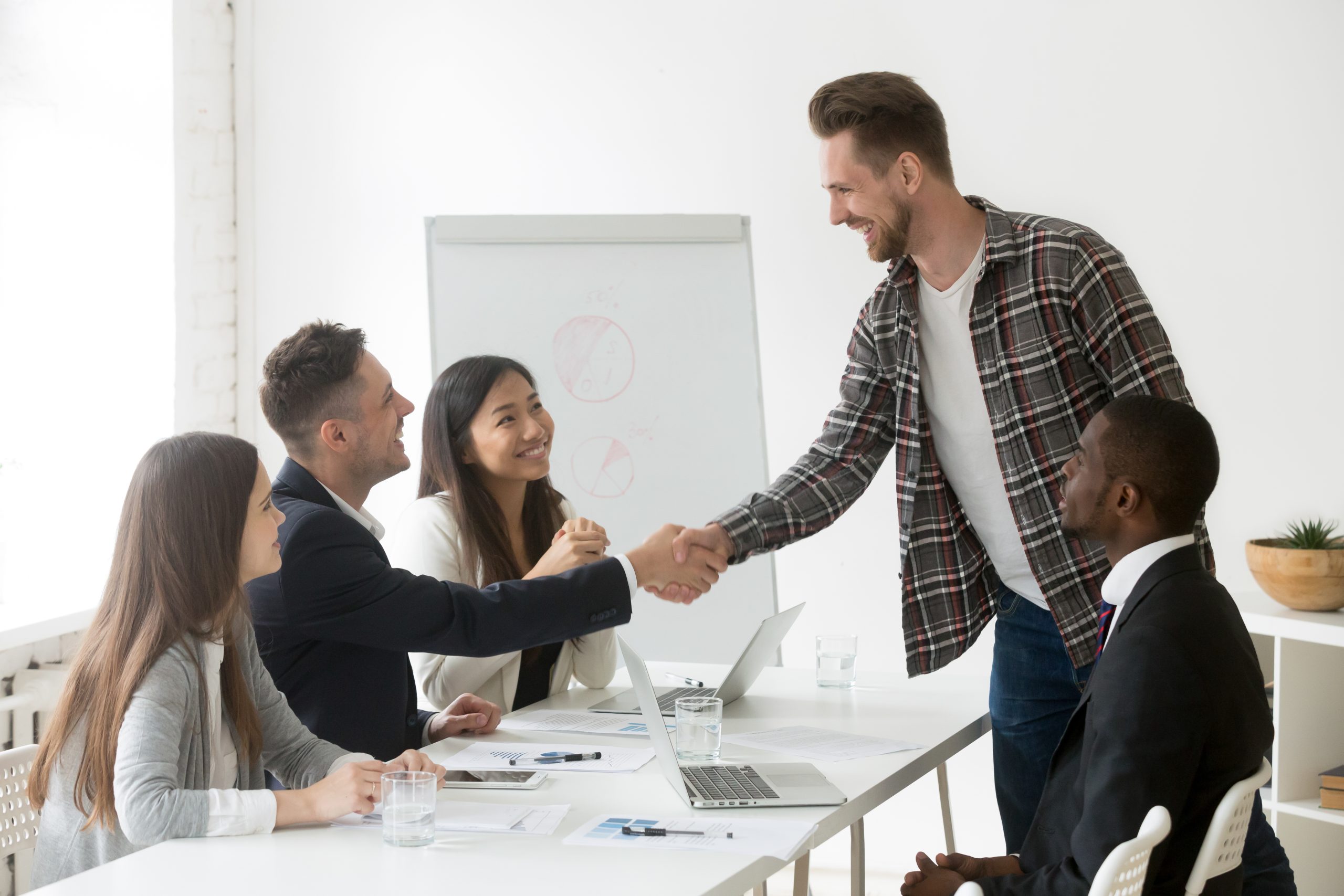 Office meeting with 2 people shaking hands, smiling along with others. Benefits of Gratitude-Hope and Belief.